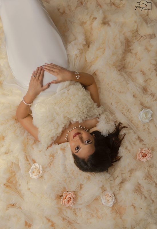 Expectant mother lying among cream feathers and roses